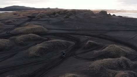 Motorbike-rider-cruising-through-black-sand-dunes-in-Iceland,-extreme-sport,-sunrise