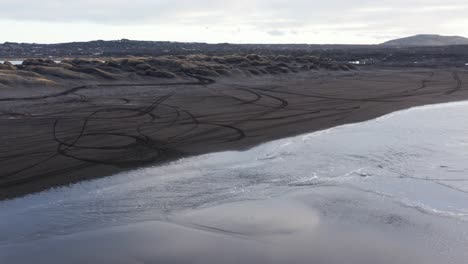 Low-tide-at-Sandvik-black-volcanic-beach-in-Iceland,-reflection-of-sky-on-wet-sand,-aerial