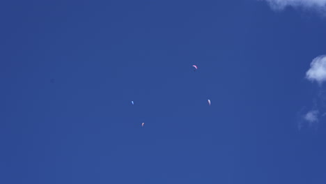 Cuatro-Paracaídas-Vuelan-Alto-En-Un-Cielo-Azul-Con-Algunas-Nubes-Sobre-Los-Alpes-Suizos,-Engelberg,-Obwalden
