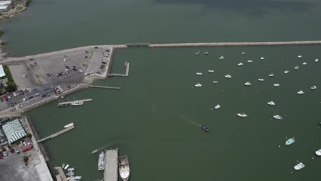 Aerial-view-overlooking-the-harbor-and-a-lot-of-anchored-boats-in-sunny-Plymouth,-USA---tracking,-tilt,-drone-shot