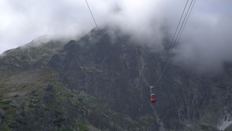Tiny-red-gondola-slowly-passes-between-mountain-peaks-into-the-clouds