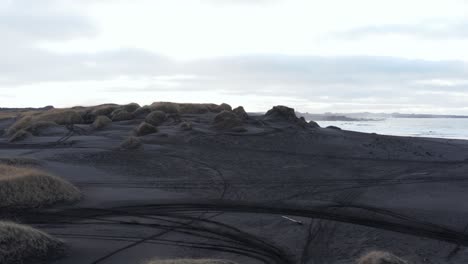 Grassy-dunes-with-volcanic-black-sand-in-Sandvik-coastal-cove,-aerial