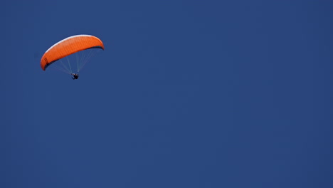 An-orange-parachute-floats-in-a-blue-sky-in-the-middle-of-the-day,-above-the-Swiss-Alps,-Obwalden
