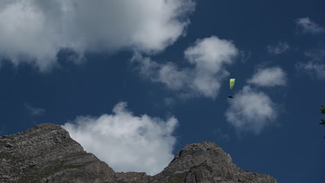 A-yellow-parachute-is-flying-over-rocky-mountain-peaks-in-the-swiss-alps-in-a-cloudy-sky,-Engelberg,-Obwalden