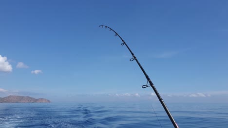 A-solo-fishing-rod-trolling-on-a-moving-boat-against-a-blue-sky-and-ocean-backdrop-on-a-perfect-day-with-fine-weather-and-calm-sea-conditions