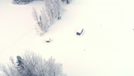 Aerial-drone-forward-moving-shot-over-a-rectangular-vacation-cabin-surrounded-by-white-snow-on-a-cold-winter-day
