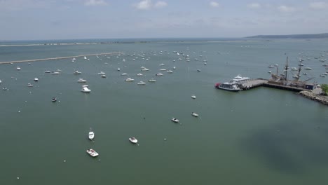 Aerial-view-over-anchored-boats,-passing-the-Mayflower-II-in-sunny-Plymouth,-USA