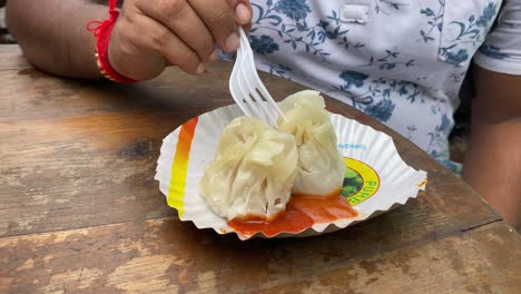 Front-view-Of-man-eating-freshly-baked-Momo-packed-with-chicken-mince-on-a-street-in-Tiretta-Bazar,-Kolkata,-with-a-plastic-fork