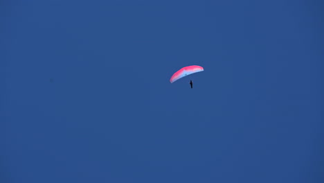 A-pink-and-blue-parachute-is-flying-alone-in-a-bright-blue-sky-over-the-alps,-Switzerland,-Engelberg