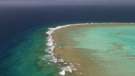 High-aerial-fly-over-of-shallow-reef-system-in-Tonga-meeting-the-deep-blue-pacific-ocean