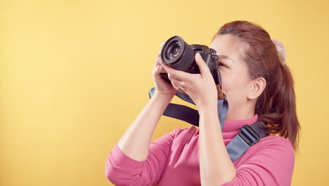 Smart-Happy-delighted-an-Asian-woman-with-a-digital-camera-and-isolated-yellow-background