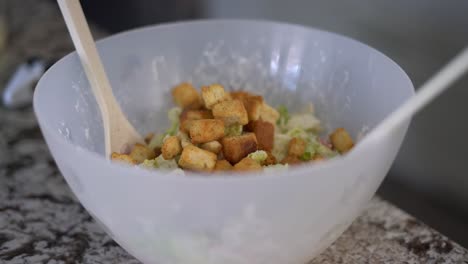 Adding-crunchy-croutons-to-large-bowl-of-caesar-salad,-close-up-selective-focus