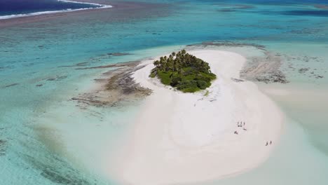 Aerial-pull-back-over-small-sandy-island-with-palm-trees-to-pan-up-reveal-of-expansive-blue,-shallow-reef-in-Tonga