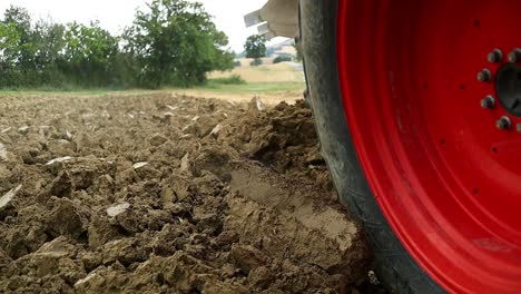 A-Plowing-soil-tractor-driving-by-plowing-up-dirt-from-the-ground-on-a-farm,-static-close-up