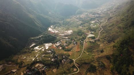 A-wide-aerial-shot-panning-above-two-cable-cars-as-they-journey-high-above-a-huge-farming-valley-in-Sapa-Vietnam