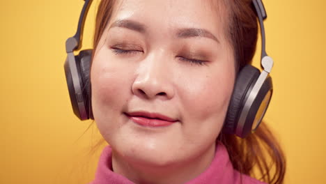 Nahaufnahme-Einer-Jungen-Asiatischen-Frau,-Die-Ein-Digitales-Tablet-Verwendet,-Um-Fröhlich-Musik-über-Kopfhörer-Zu-Hören,-Entspannt-Auf-Hellgelbem-Hintergrund