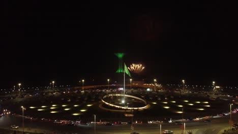 Noche-Con-Fuegos-Artificiales,-Bandera-De-Arabia-Saudita-Ondeando,-Torre-Khobar-En-El-Fondo