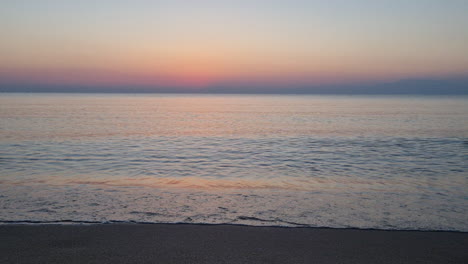 Calm-water-surface-and-sea-waves-splash-on-sandy-beach-before-sunrise