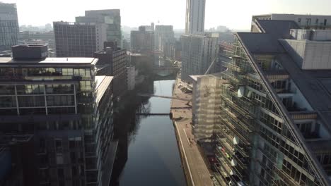 Aerial-drone-flight-above-the-rooftops-along-the-River-Irwell-in-Manchester-City-Centre-shoing-a-sunny-and-hazy-view-of-the-skyline