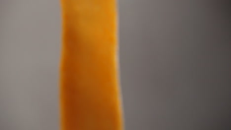 Close-up-of-a-very-thin-strip-of-orange-sweet-potato,-moving-in-front-of-the-camera-in-slow-motion-shot