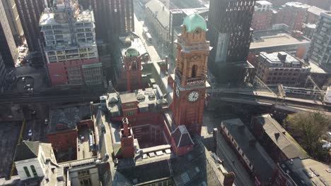 Aerial-drone-flight-over-the-rooftop-of-the-Refuge-Building-on-Oxford-Road-in-Manchester-City-Centre-with-the-camera-panning-down-to-slowly-reveal-a-birdseye-view-of-the-Clock-Tower-and-Train-Station