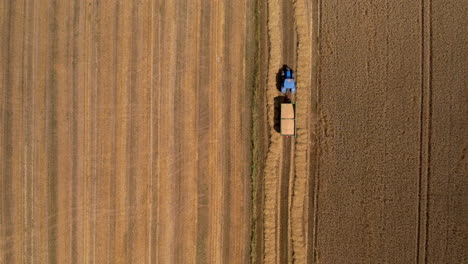 Agriculture-Machinery-and-Hay-Harvest,-Tractor-in-Agricultural-Farmland-Field-Passing-Driving-Carry-Transporting-Hay-Bales,-Aerial-Top-Down-View-of-Farm-Work