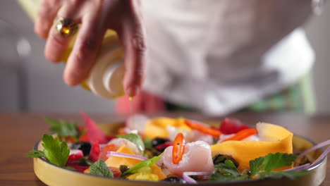 Chef-with-a-white-shirt-prepares-a-sea-bass-carpaccio-and-puts-olive-oil-on-it---slow-motion-push-in-to-focus-shot