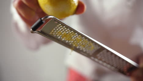 Close-Up-Shot-of-a-Professional-Chef-Grating-Lemon-on-a-dish,-slow-motion-shot,-blurred-white-background