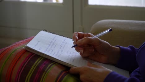 Adult-Female-Student-At-Home-Taking-Notes-During-Online-Course