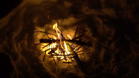 Person-Adding-Logs-to-a-Fire-in-a-Hole-in-the-Snow-during-a-Cold-Winter-Night-in-the-Alps