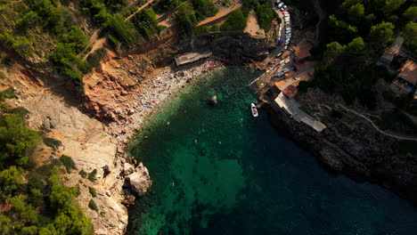 Dramatic-aerial-tilt-down-of-secluded-Mediterranean-cove-and-beach-with-people-swimming-and-rowing-boats