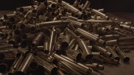 Extreme-close-zoom-out-of-large-pile-of-bullet-cases-on-a-wooden-surface