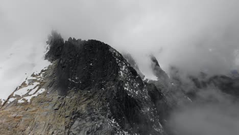 Aerial-view-entering-the-fog-with-a-rocky-and-sharp-ridge-in-the-Andes-on-a-cloudy-day