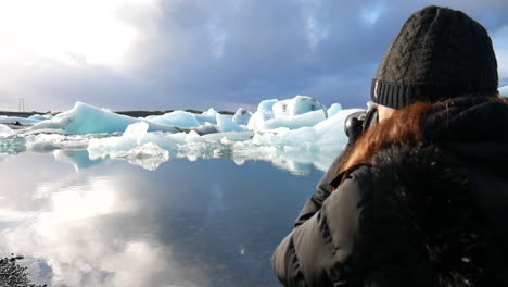 Cinematic-shot-of-a-woman-taking-photos-of-the-landscape-and-the-icebergs-found-in-the-Jökulsárlón-national-park-in-Iceland