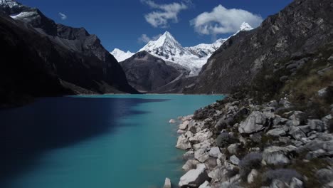 Cinematic-aerial-shot-entering-a-valley-over-a-blue-lagoon-and-a-snow-capped-peak-at-Laguna-Parón