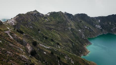 Vista-Aérea-De-Las-Laderas-De-Las-Montañas-Con-Una-Laguna-Azul-En-El-Lago-Quilotoa,-Ecuador