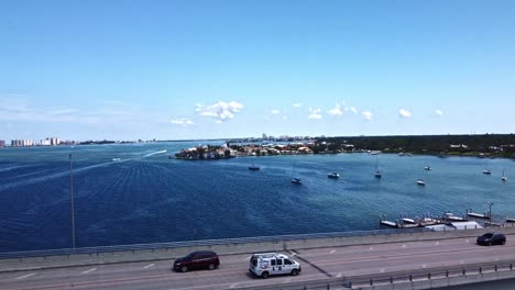 The-Bellaire-Causeway-bridge-in-Belleair-Beach,-Florida,-USA,-has-many-cars-travelling-on-both-lanes-while-it-is-flanked-by-a-blue-sea-and-a-far-off-township