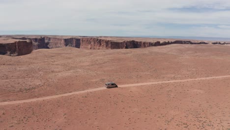 Aerial,-van-life-camper-van-on-a-road-trip-driving-on-dry-red-desert-road-in-Utah