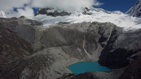 Aerial-shot-with-a-frozen-glacier-and-a-blue-lake-with-rocky-mountains-at-Laguna-69-in-the-Andes,-Peru