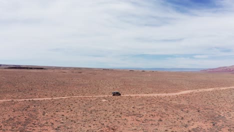 Aerial,-van-life-camper-van-driving-on-dry-red-desert-road-in-Arizona