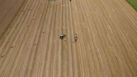 Hay-Harvest-Agriculture-Machinery,-Tractor-in-Agricultural-Farmland-Field-Working-Carry-Load-Hay-Bales,-Aerial-View-of-Farm-Work