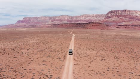 Camper-van-on-a-road-trip-driving-on-single-desert-dirt-road-in-Utah,-aerial