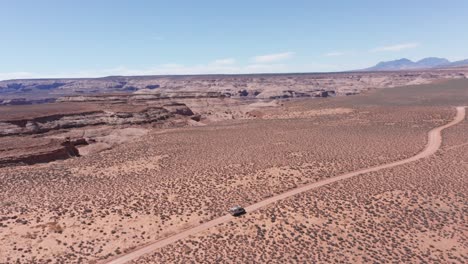 Aerial,-camper-van-on-road-trip-driving-on-vast-red-desert-in-Arizona