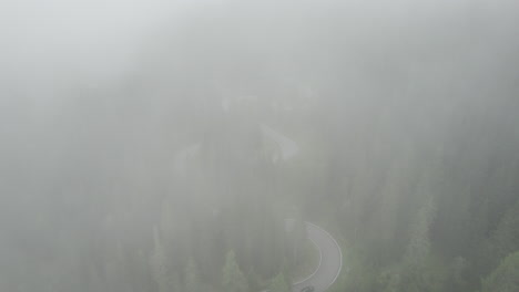 Car-on-winding-alpine-road-through-misty-spruce-forest,-Giau-Pass