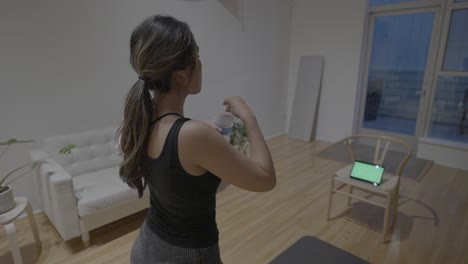 A-following-action-shot-of-an-Hispanic-woman-finishing-up-her-workout-and-saying-goodbye-to-her-trainer,-our-friends-in-her-green-screened-tablet-while-stretching-in-her-living-room