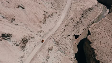 Orange-suv-driving-on-canyon-road-next-to-gorge,-aerial-tracking-shot