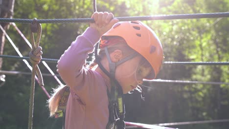 Young-girl-challenging-herself-in-climbing-park---Beautiful-sun-backlight-with-solar-flare-and-girl-moving-ahead-in-slow-motion---6-year-old-female-european-with-safety-equipment