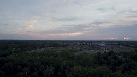 Aerial-drone-forward-moving-shot-over-a-lumber-mill-during-evening-time-with-sunset-over-the-horizon