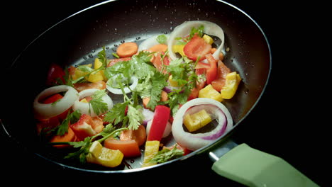 Slow-rotating-frying-pan-full-of-chopped-vegetables-on-black-background