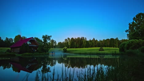 Steam-rises-off-the-warm-pond-water-by-a-cabin-in-the-countryside-as-the-moon-rises---time-lapse
